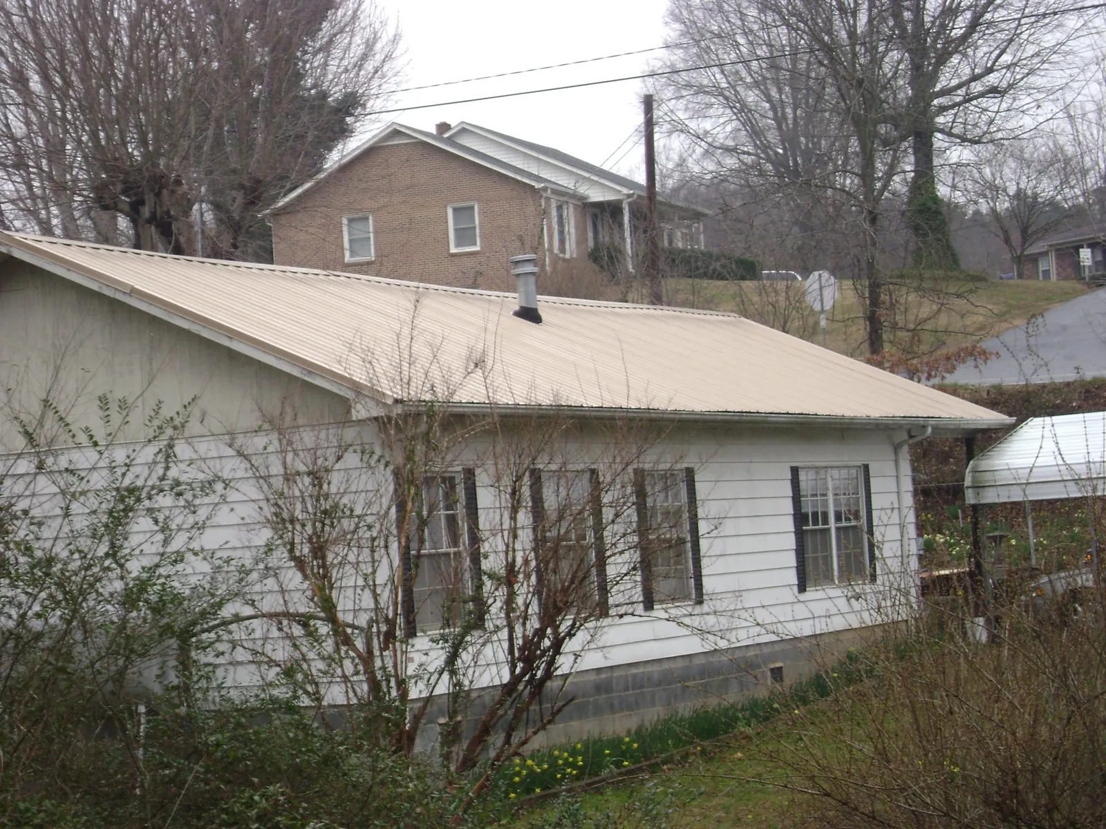 Tan metal roof on a white sided house set into a hillside — Commercial Roofing by Roofing Brothers in Mapleton